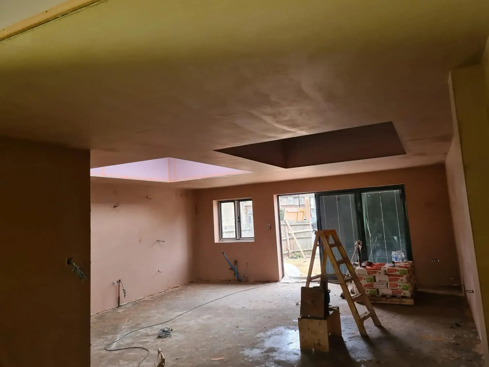 Freshly plastered walls and ceiling in an open-plan room extension with two roof lanterns and wide glazed doors.