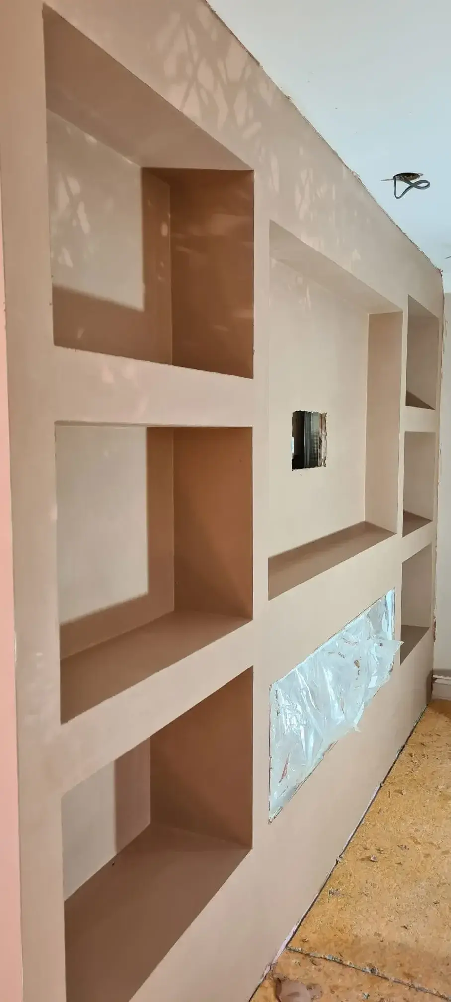 Plasterboard feature wall built with square recessed shelving openings, skimmed and ready for decorating.