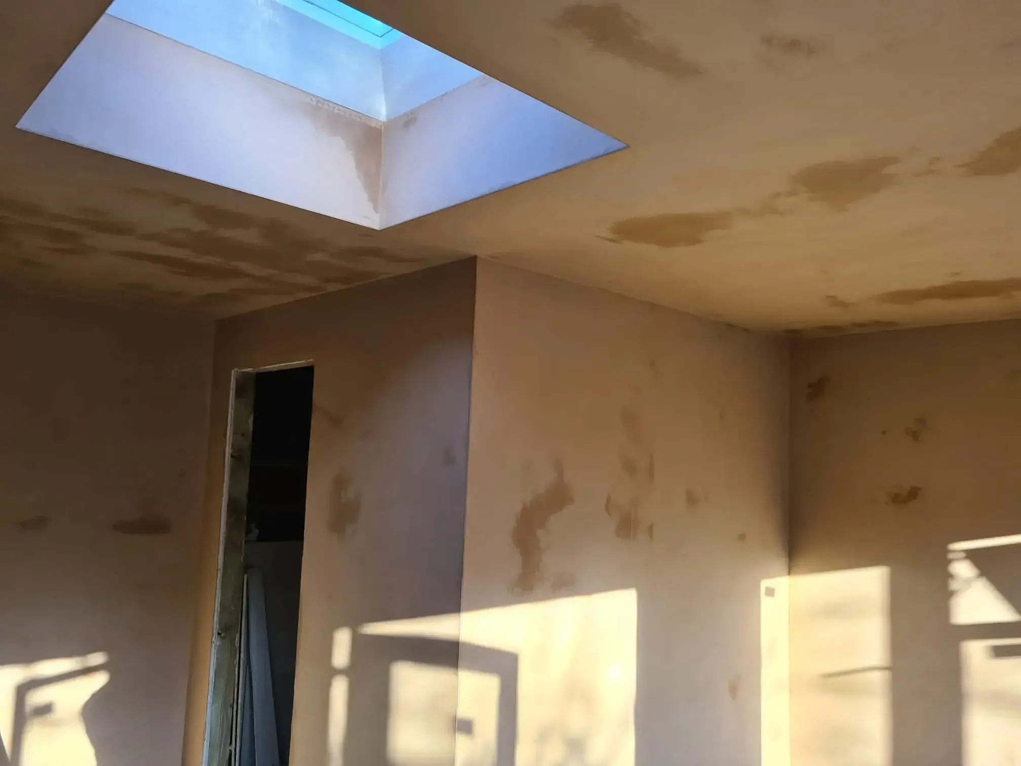 Plastered ceiling and the angled reveal of a roof light, with a squared internal corner in daylight.